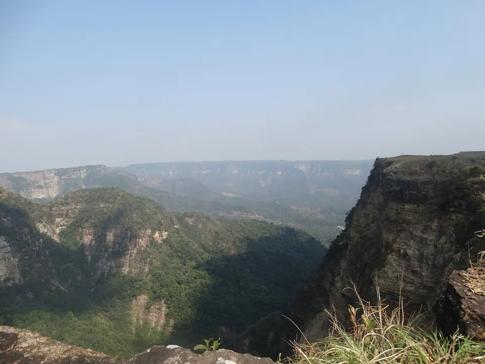 Sheer cliffs dropping into the forested Balpakram canyon under a hazy sky, South Garo Hills