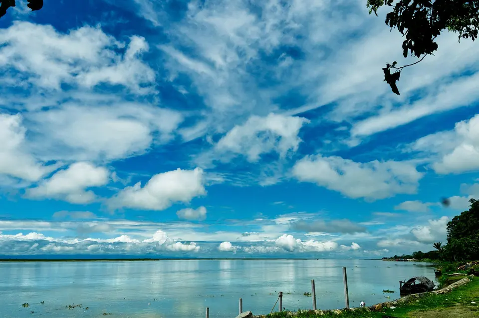 Wisps of white cloud over the wide, calm Brahmaputra seen from its bank at Dibrugarh