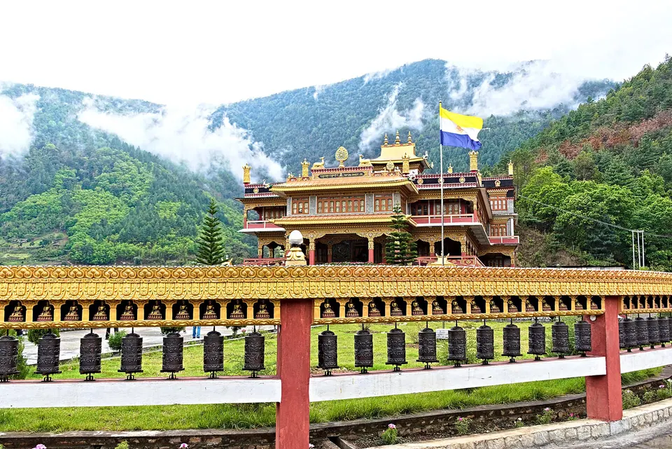 Thupsung Dhargye Ling monastery behind a row of prayer wheels, with cloud on the hills of Dirang