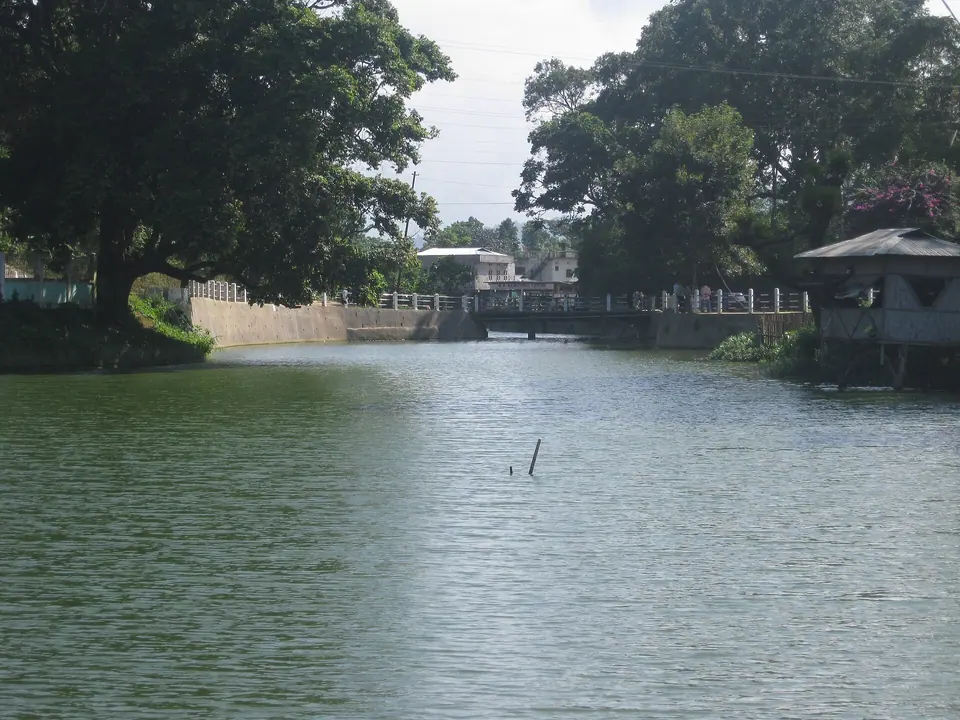 The calm waters of Haflong Lake framed by large trees and a small footbridge
