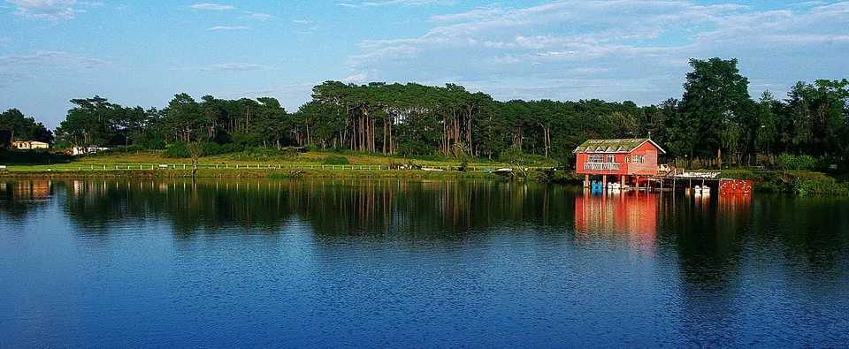 Thadlaskein Lake near Jowai reflecting a red-roofed boathouse and a line of tall trees