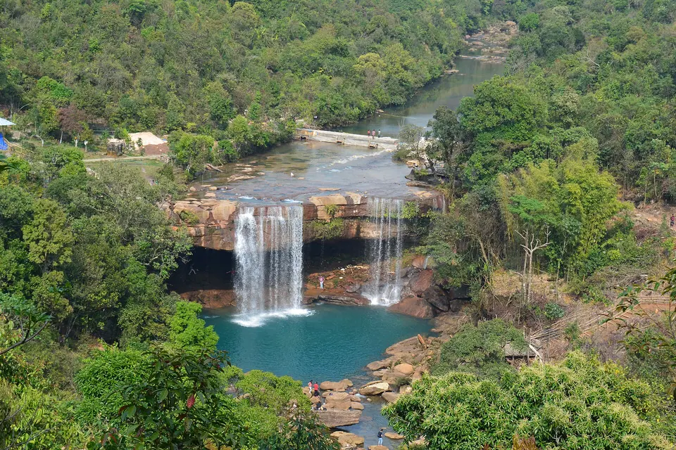 Krang Suri Falls seen from the hilltop, twin streams dropping into a blue pool in thick forest