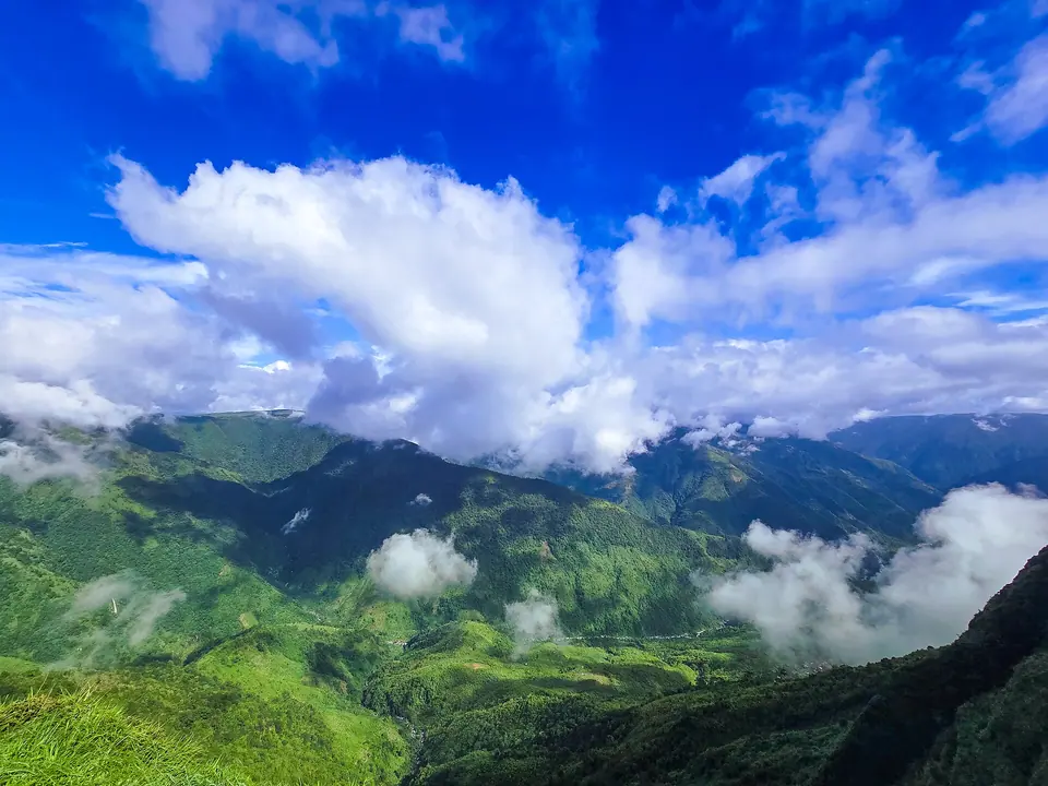 Monsoon clouds drifting through the green valleys below the Laitlum rim under a bright blue sky