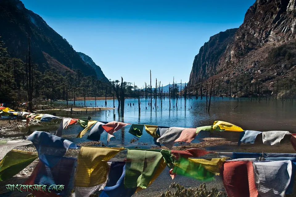 Prayer flags strung along the shore of Sangetsar (Madhuri) Lake below sunlit cliffs