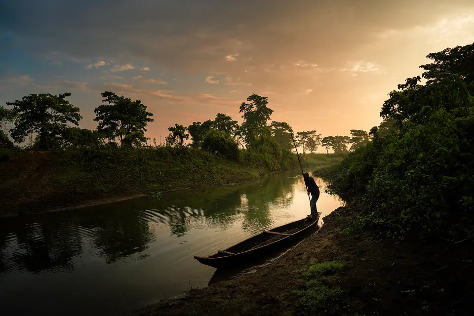 A boatman poling a wooden canoe along a quiet channel at sunrise on Majuli