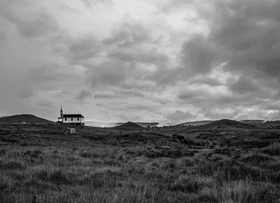 Black-and-white view of a lone church on the grassy uplands of Mawsynram under heavy rain clouds