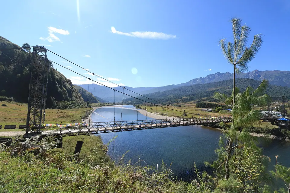A suspension bridge over the blue Siyom river in the wide Mechuka valley under a clear sky