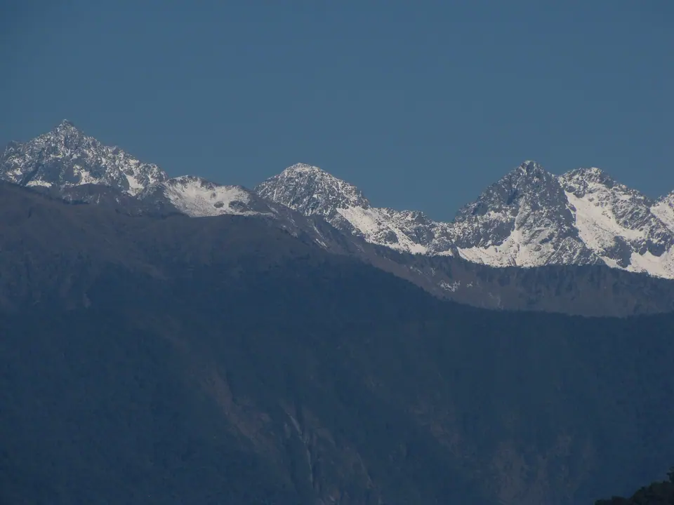 Snow-covered Himalayan peaks above dark forested ridges, seen from the trail into Namdapha