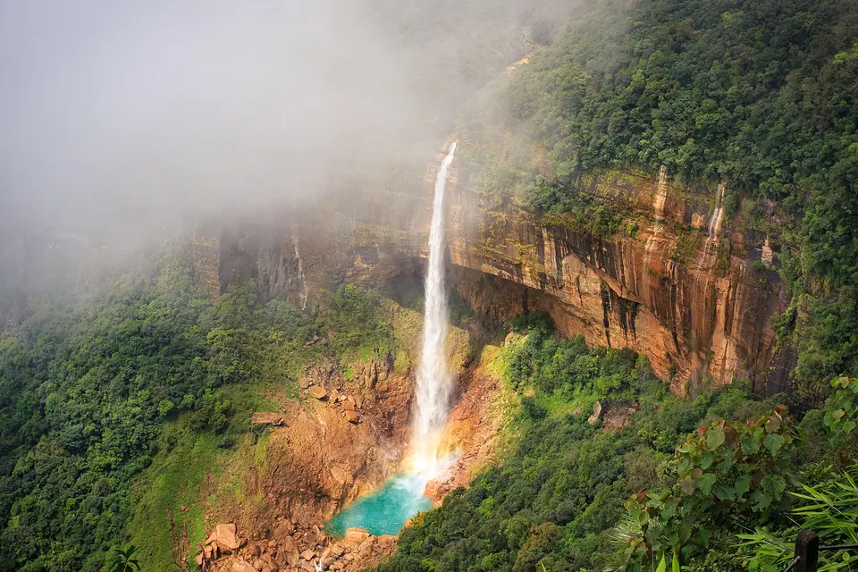 Mist rolling over the cliffs as Nohkalikai Falls drops into its turquoise plunge pool