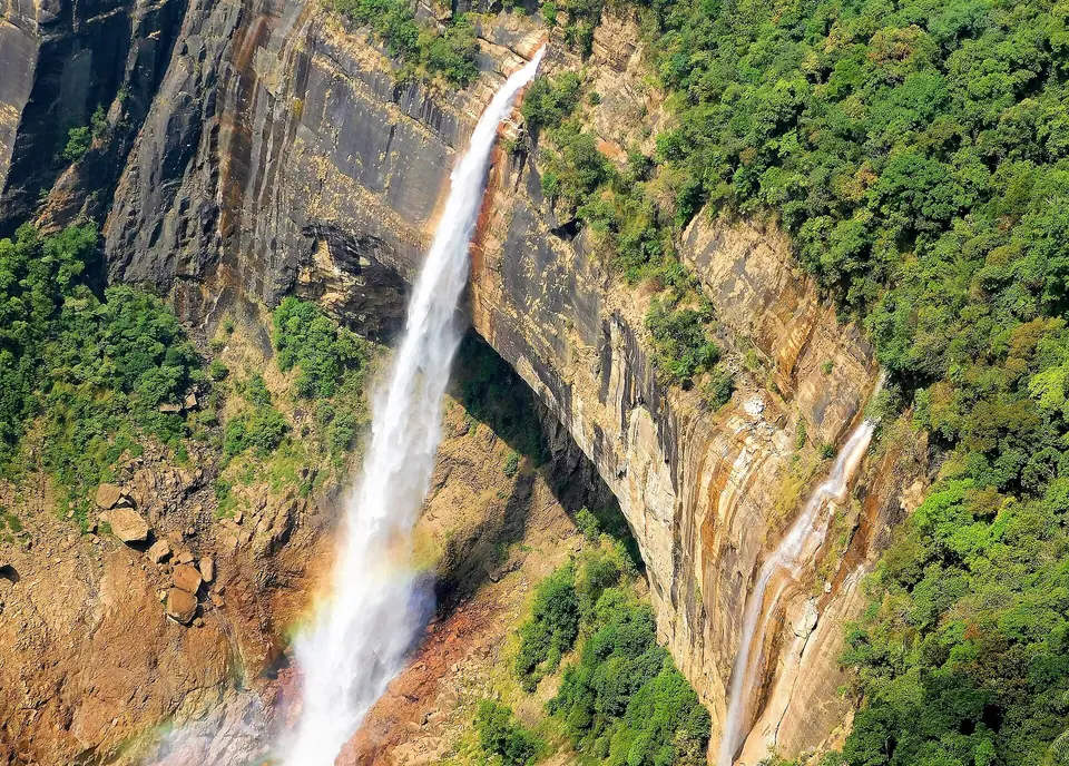 Close view of Nohkalikai Falls pouring down a streaked sandstone cliff with a faint rainbow