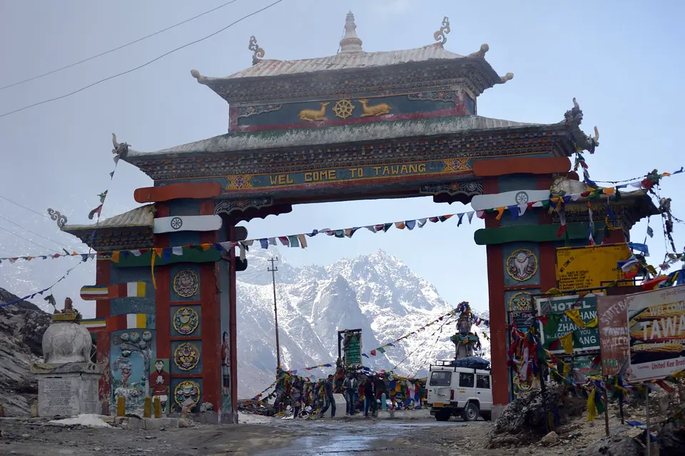 The painted Tawang gateway at Sela Pass with prayer flags and snowy peaks behind