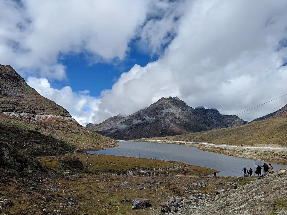 Walkers beside Sela Lake in October, with a rocky summit and white clouds above
