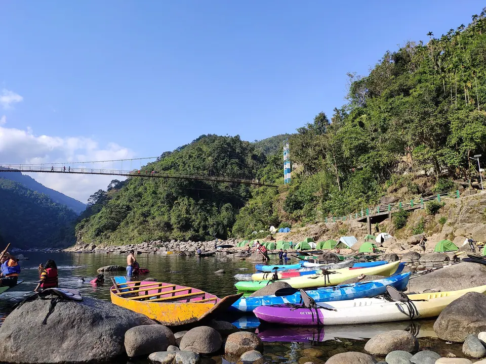Kayaks and wooden boats moored on the rocky bank of the Umngot River below green hills