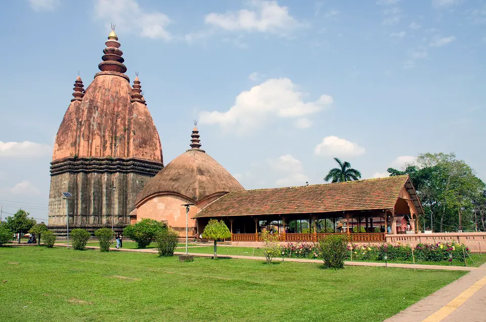 The tall brick spire of Shiva Dol beside smaller shrines and a long hall on green lawns, Sivasagar