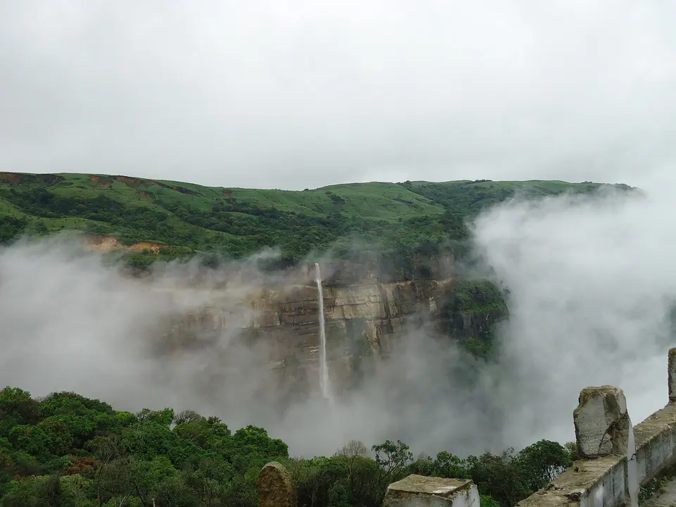 A tall waterfall dropping off a green plateau edge into a sea of cloud near Sohra (Cherrapunji)