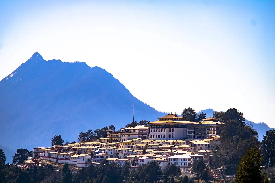 Tawang Monastery's white buildings and gold roofs spread along a ridge below a blue peak