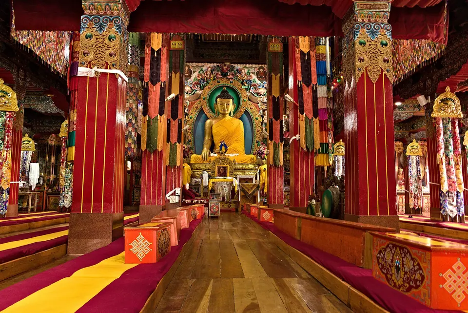 Red pillars and rows of seating leading to the golden Buddha in Tawang Monastery's main hall