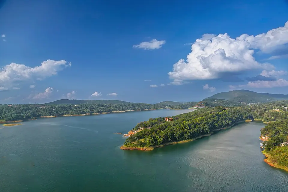 Blue waters of Umiam Lake wrapping around forested islands and ridges under white clouds