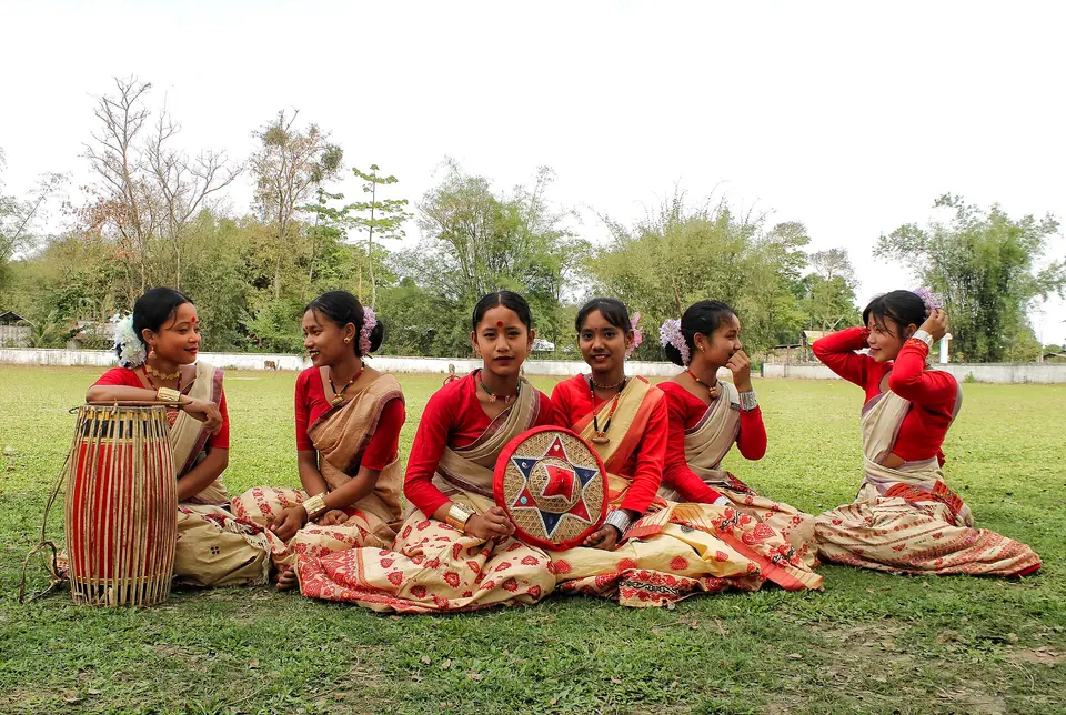 Young Bihu dancers in muga silk resting on the grass beside a dhol drum, Lakhimpur
