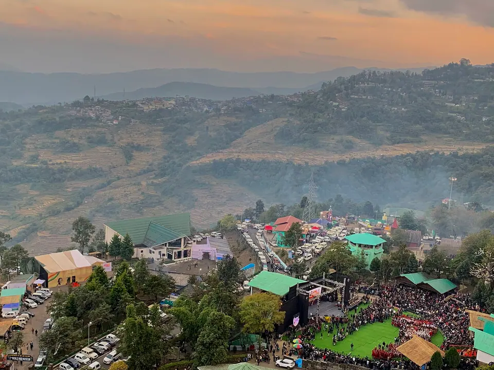 The Kisama heritage village and main arena of the Hornbill Festival among forested hills at dusk